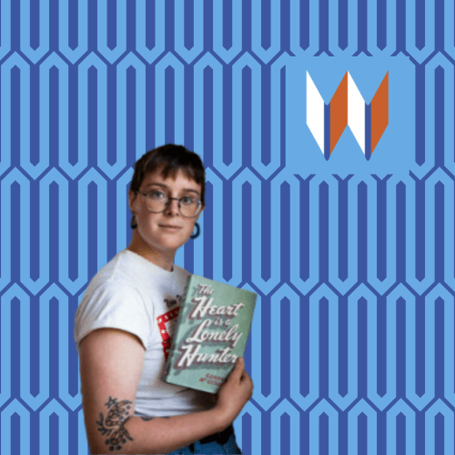 Sarah, The Palouse Library Branch Manager, Stands In Front Of A Blue Patterned Background, Holding A First Edition Copy Of The Heart Is A Lonely Hunter By Carson McCullers.