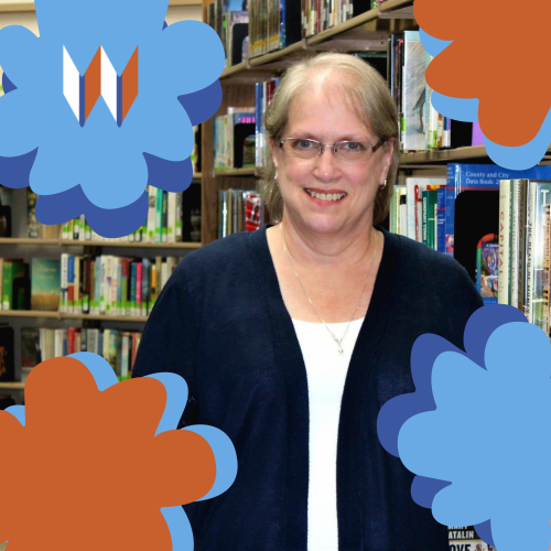 Joanne, Our Circulation Specialist, Poses In Front Of Books, Surrounded By Orange And Blue Flowers.